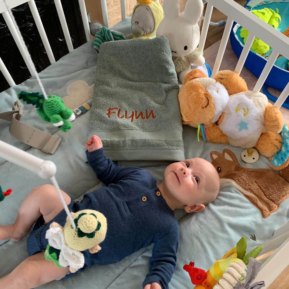 Schattige baby liggend naast een zachte babyhanddoek met met de hand geborduurde naam – De Mokkes